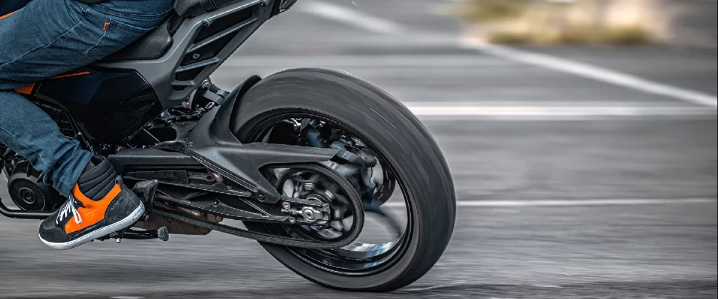 Detailaufnahme des Hinterrads einer KTM 125 DUKE 2026 in einer Kurve – Fahrerfuß und Kettenantrieb sichtbar