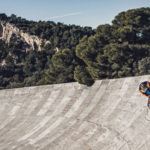 Ein KTM Motorradfahrer fährt mit hoher Geschwindigkeit auf einer geneigten Rennstrecke in einer malerischen Landschaft.