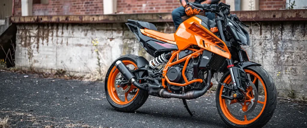 KTM 390 Duke in Orange vor einer Fabrikhalle mit Fahrer.