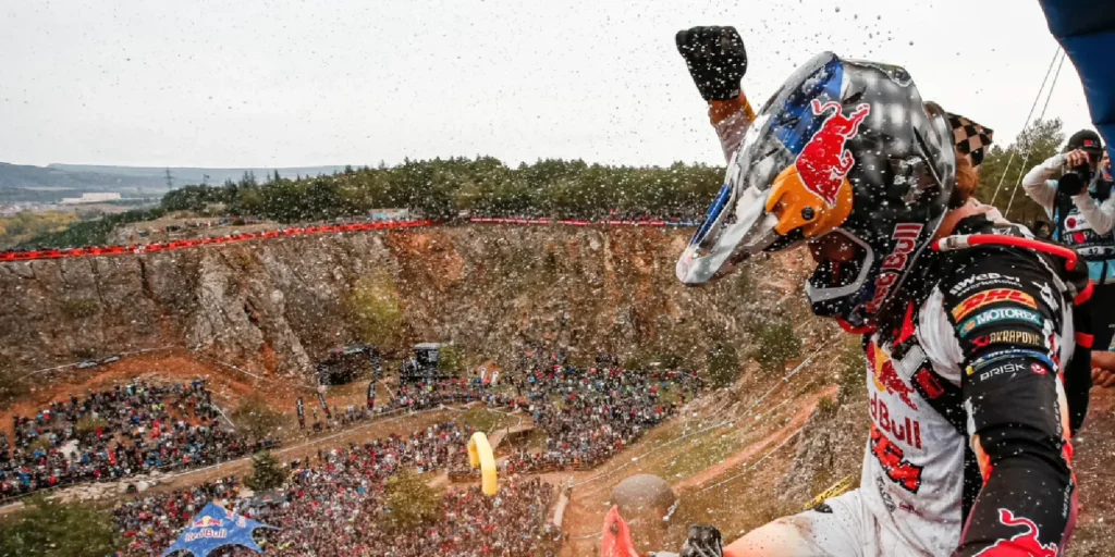 Enduro-Fahrer in Kini Red Bull Design fliegt durch eine spektakuläre Wasserfontäne