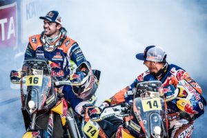 Zwei KTM-Fahrer in Rennmontur feiern auf ihren Motorrädern inmitten von Rauch und Jubel.